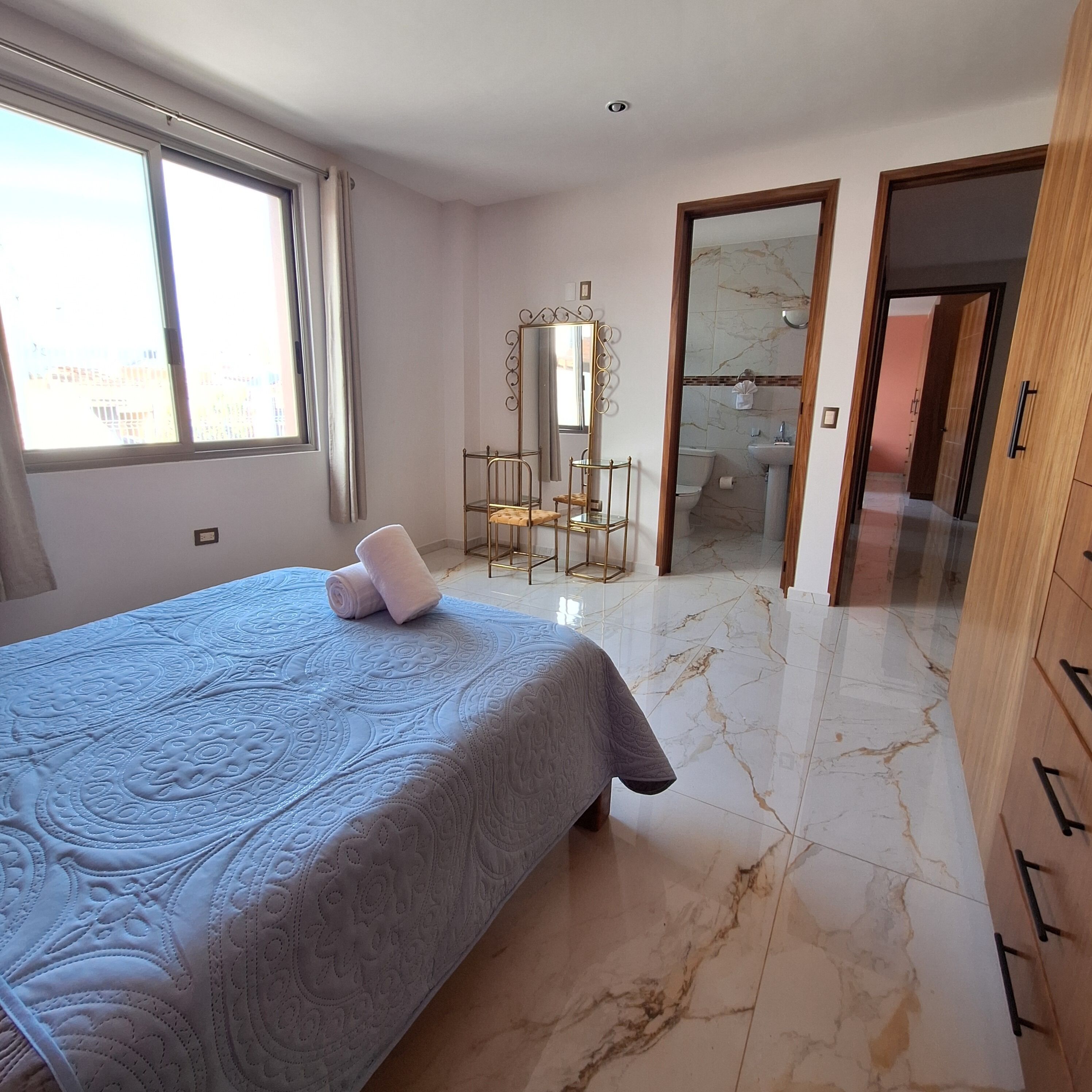 Un dormitorio con cama, tocador y baño visible a través de una puerta abierta.