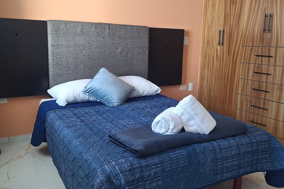 Ein Schlafzimmer mit Bett, Kissen, einem Holzschrank und Fliesenboden.