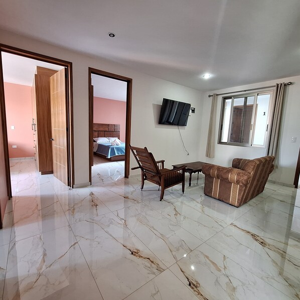 A spacious living area with a sofa, a wooden table, and a TV mounted on the wall. - Depas Ocampo de Grupo Casa Mariano (Morelia)