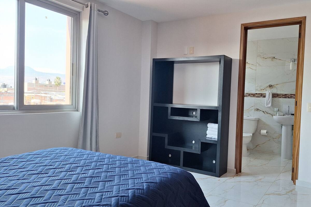 Ein Schlafzimmer mit Bett, Schrank und einem Badezimmer mit Waschbecken, mit Blick nach außen.