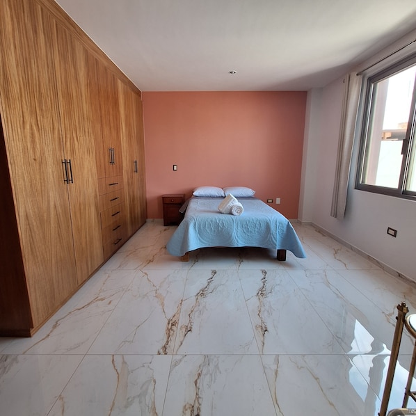 A bedroom with a bed, wooden wardrobe, and a window.