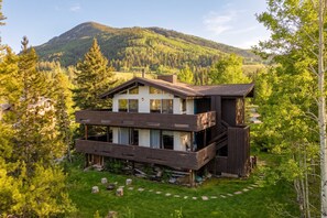 A modern two-story house with a deck, surrounded by a forest and a mountain in the background. - Apres All Day| Mountain Views + Deck on Gore Creek (Vail)