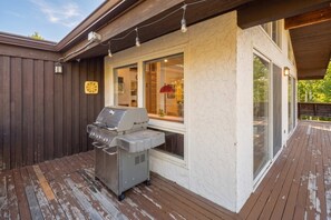 A covered outdoor area with a grill, wooden deck, and a building with large windows. - Apres All Day| Mountain Views + Deck on Gore Creek (Vail)