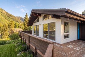 Een gebouw met twee verdiepingen, grote ramen, een houten terras en een bergachtige achtergrond.