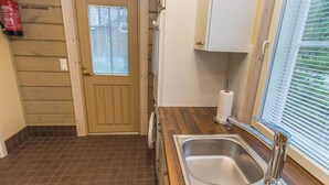 A kitchen with a wooden door, a window with blinds, a stainless steel sink, and a fire extinguisher mounted on the wall. - Villa aleksandra by Interhome (Juva)