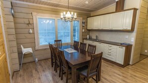 A dining area with a wooden table and chairs, a chandelier, and a kitchen with white cabinets. - Villa aleksandra by Interhome (Juva)