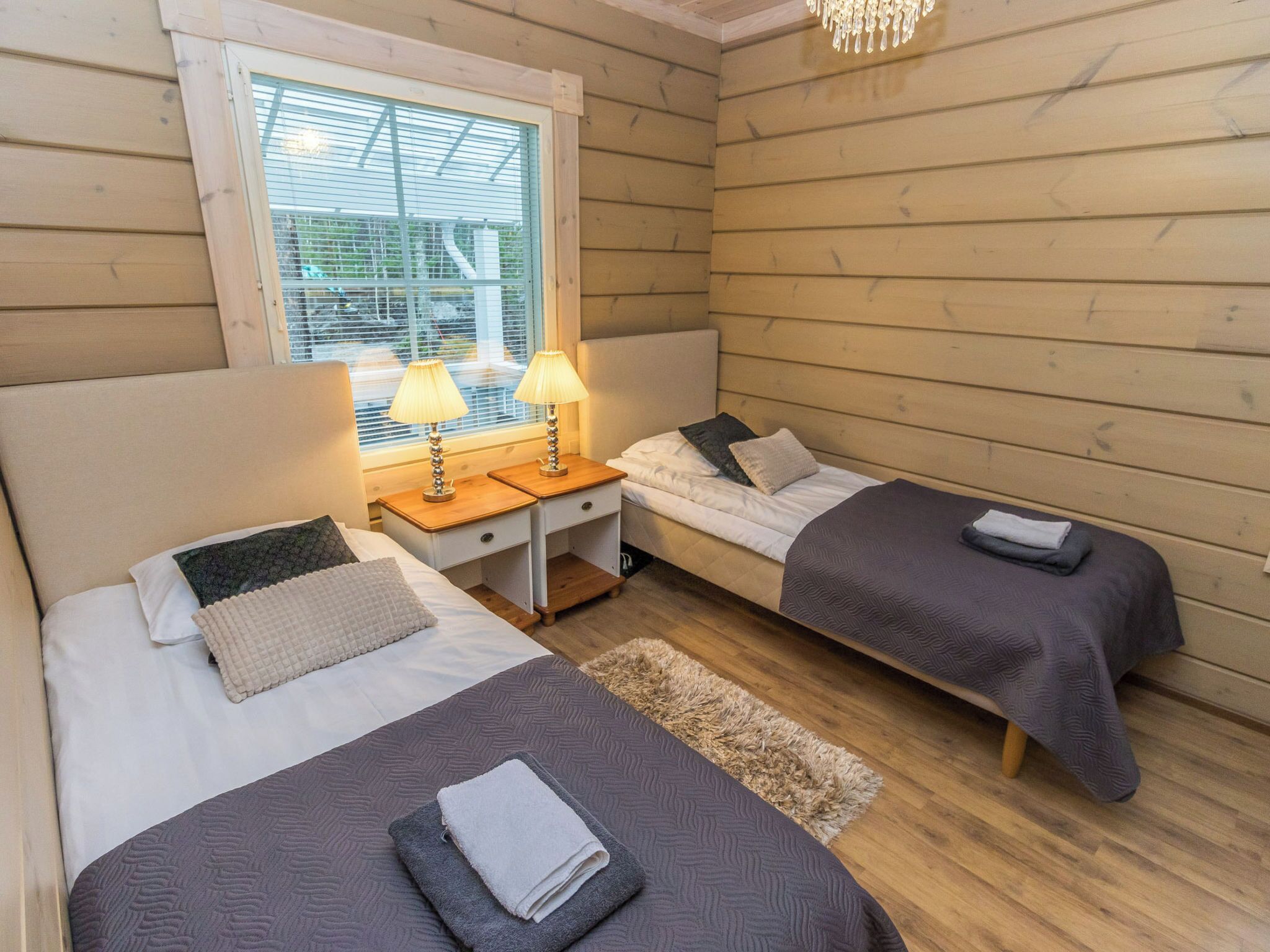 A cozy cabin-style room with two beds, a small desk, and a window with blinds.