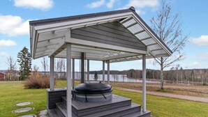 Un espace extérieur abrité avec un jacuzzi, accessible par des marches, entouré d’une pelouse verdoyante et offrant une vue sur un lac.