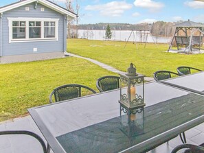 A patio with a glass table and chairs, a lantern, and a swing set in the background. - Villa kupsala by Interhome (Juva)