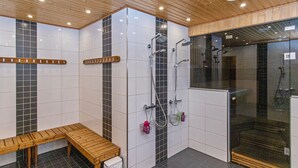 Un espace douche moderne avec un banc, une cabine de douche fermée par des parois de verre et un mur carrelé orné d’une bande noire verticale.
