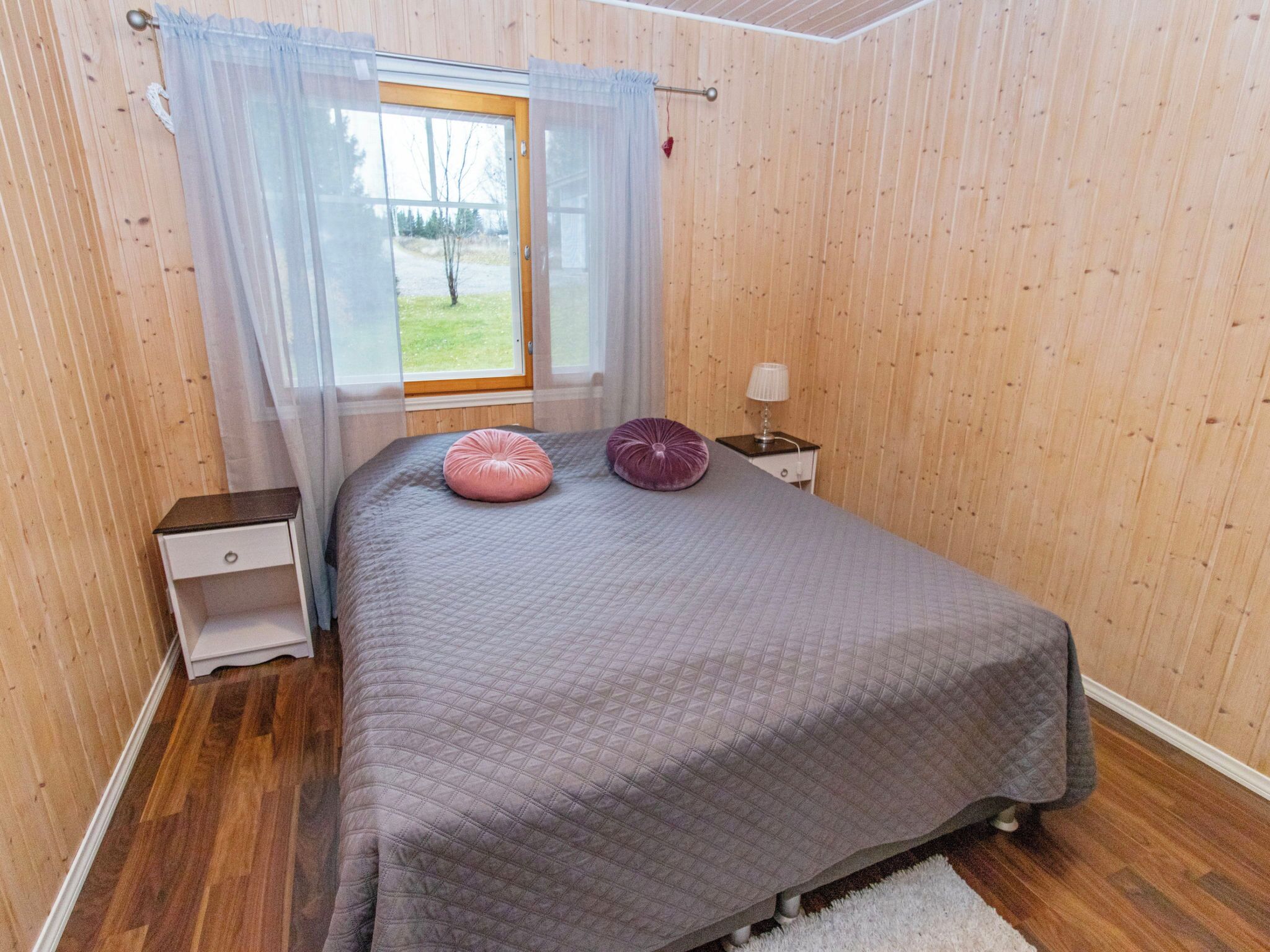 Een slaapkamer met een bed, een nachtkastje, een lamp en een raam met gordijnen.
