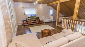 Ein geräumiges Wohnzimmer mit einem großen beigen Sofa, Holzboden, einem Fernseher und einem weißen Babybett.