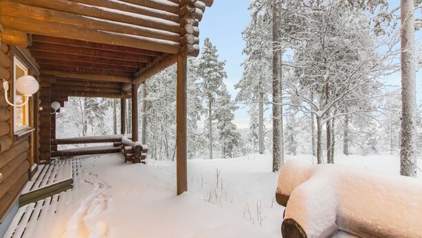 Une cabane en rondins avec un porche en bois et un paysage enneigé.