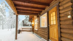 Une cabane en rondins avec une porte et des fenêtres en bois, un porche couvert et un paysage enneigé.