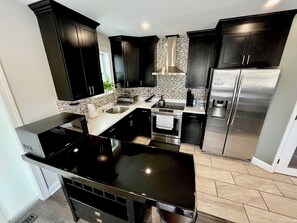 A modern kitchen with dark cabinetry, stainless steel appliances, and a black countertop. - 4BR Home with Free Parking + Outdoor Fenced Patio (Philadelphia)