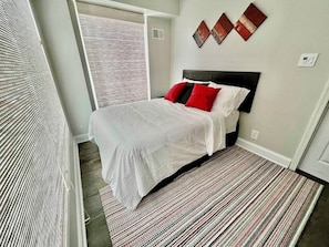 A bedroom with a bed, a patterned rug, and artwork on the wall.