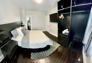 A modern bedroom with a large bed, a dark wardrobe, a TV, and a mirror. - 4BR Home with Free Parking + Outdoor Fenced Patio (Philadelphia)