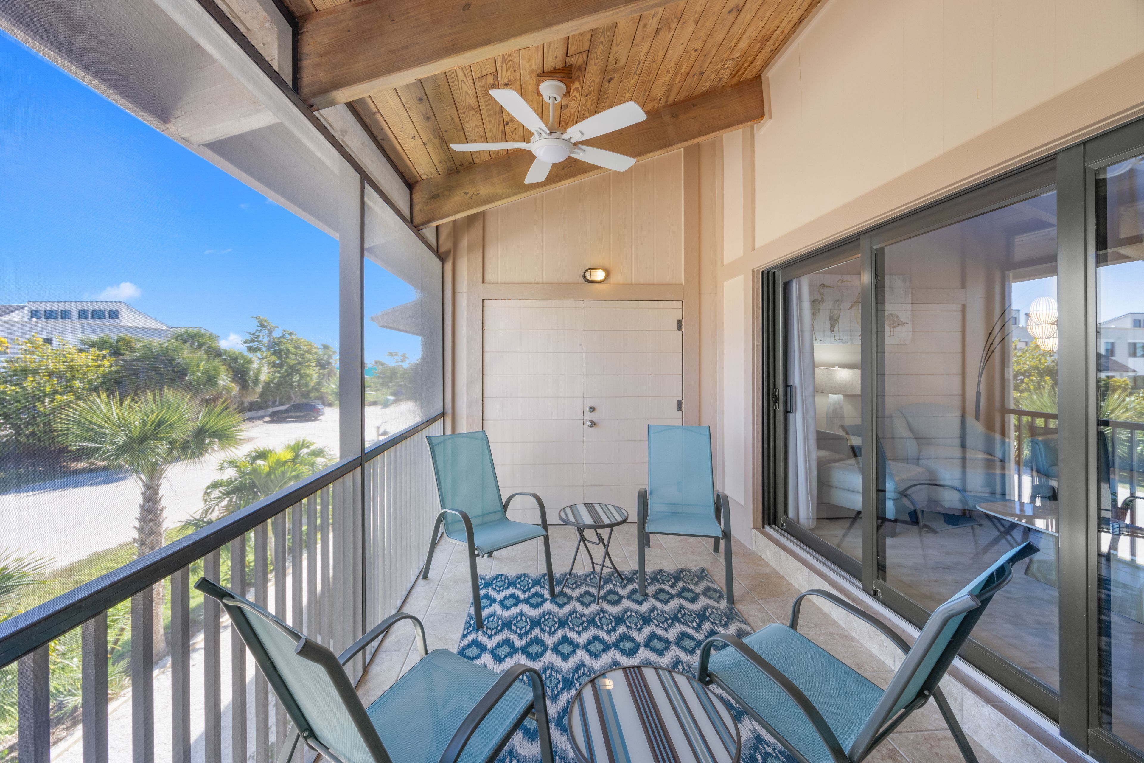 A balcony with a ceiling fan, a glass door, and a seating area with chairs and a table.