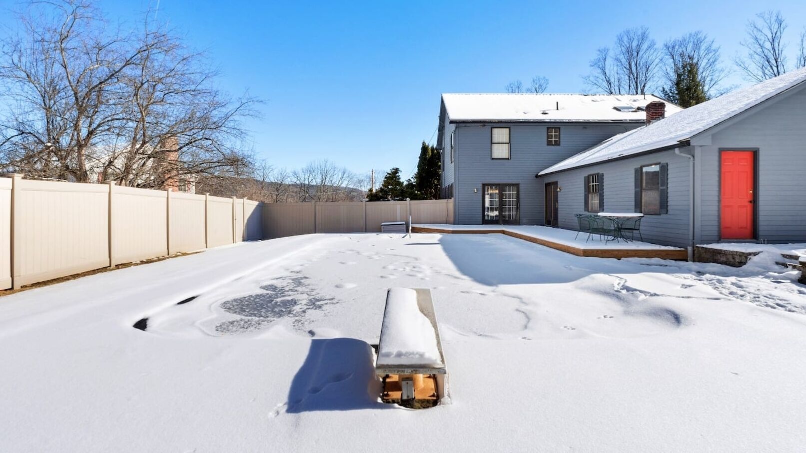 Un cortile coperto di neve con una spazzaneve, una porta rossa e una casa con facciata bianca.