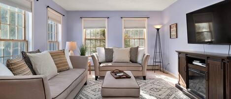 A living room with a sofa, ottoman, and a television.