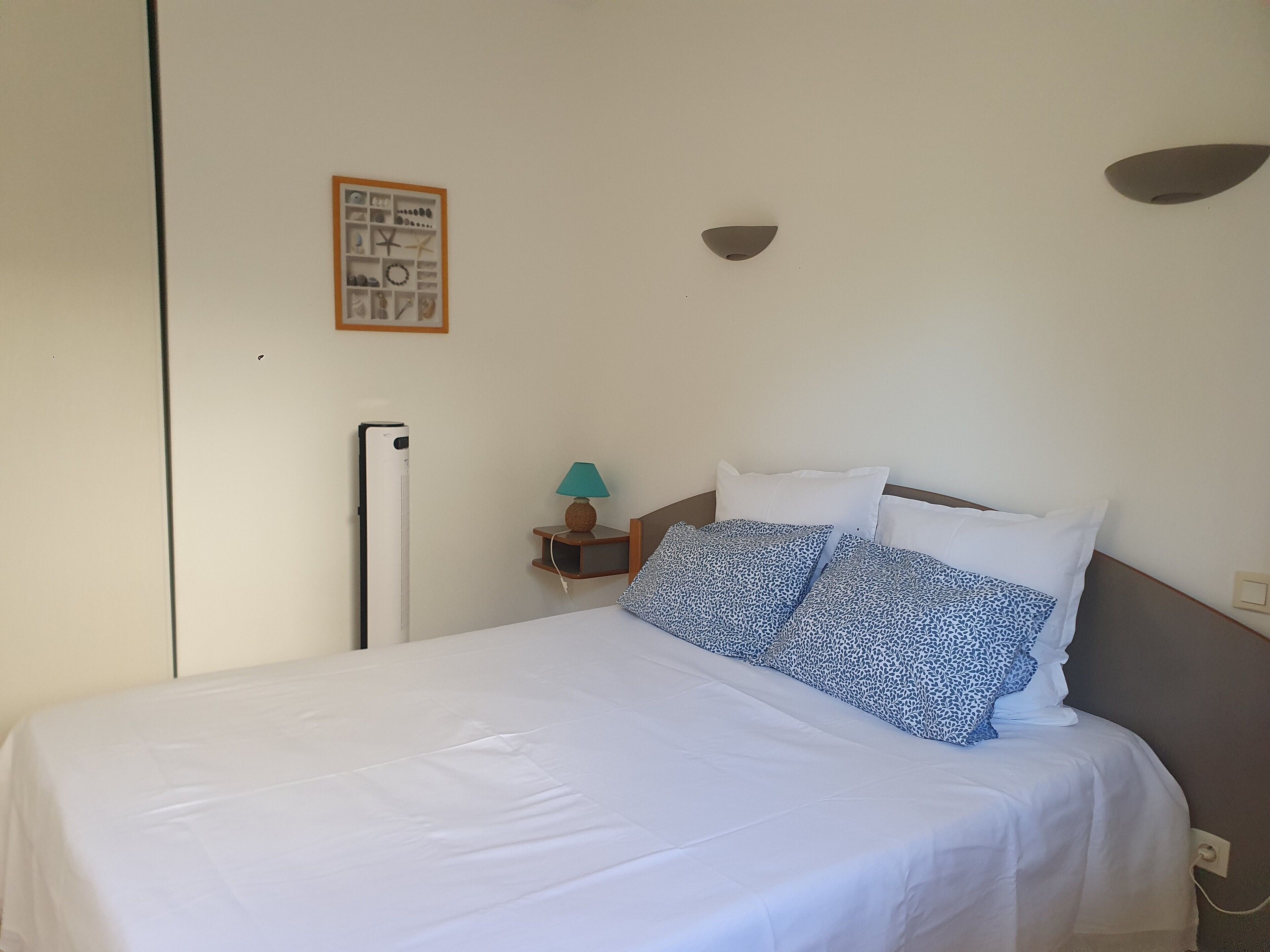 A neatly made bed with white bedding and patterned pillows, a bedside lamp, and a small framed picture on the wall.