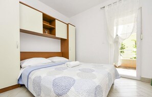 Ein Schlafzimmer mit einem Bett, einem Holzkopfstück, einer eingebauten Ablagefläche und einer Glastür, die auf einen Balkon führt.