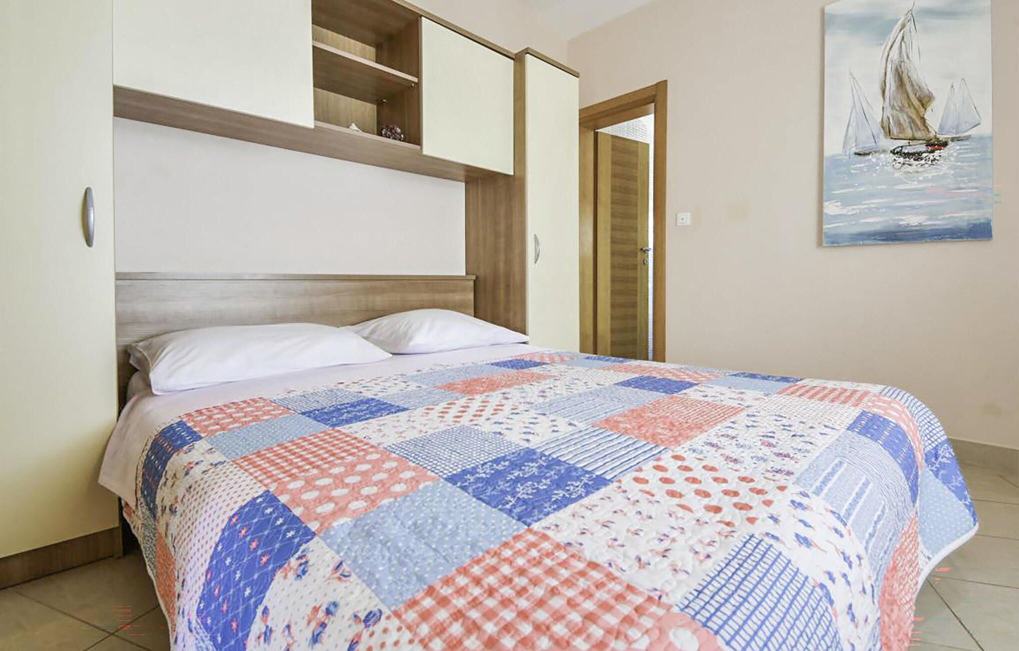 Ein Schlafzimmer mit einem Bett, einem hölzernen Kopfteil, einer eingebauten Ablage und einem Gemälde eines Segelboots an der Wand.