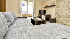 En moderne stue med sofa, fjernsyn, lille bord og en stenvæg.