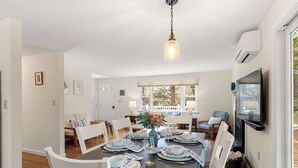 Een eetkamer met een donkerhouten tafel voor zes personen, witte stoelen en een hanglamp.
