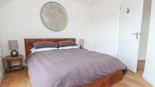 A bedroom with a wooden bed, two bedside tables with lamps, a wall-mounted decorative plate, and a white door. - Sealladh (Appin)