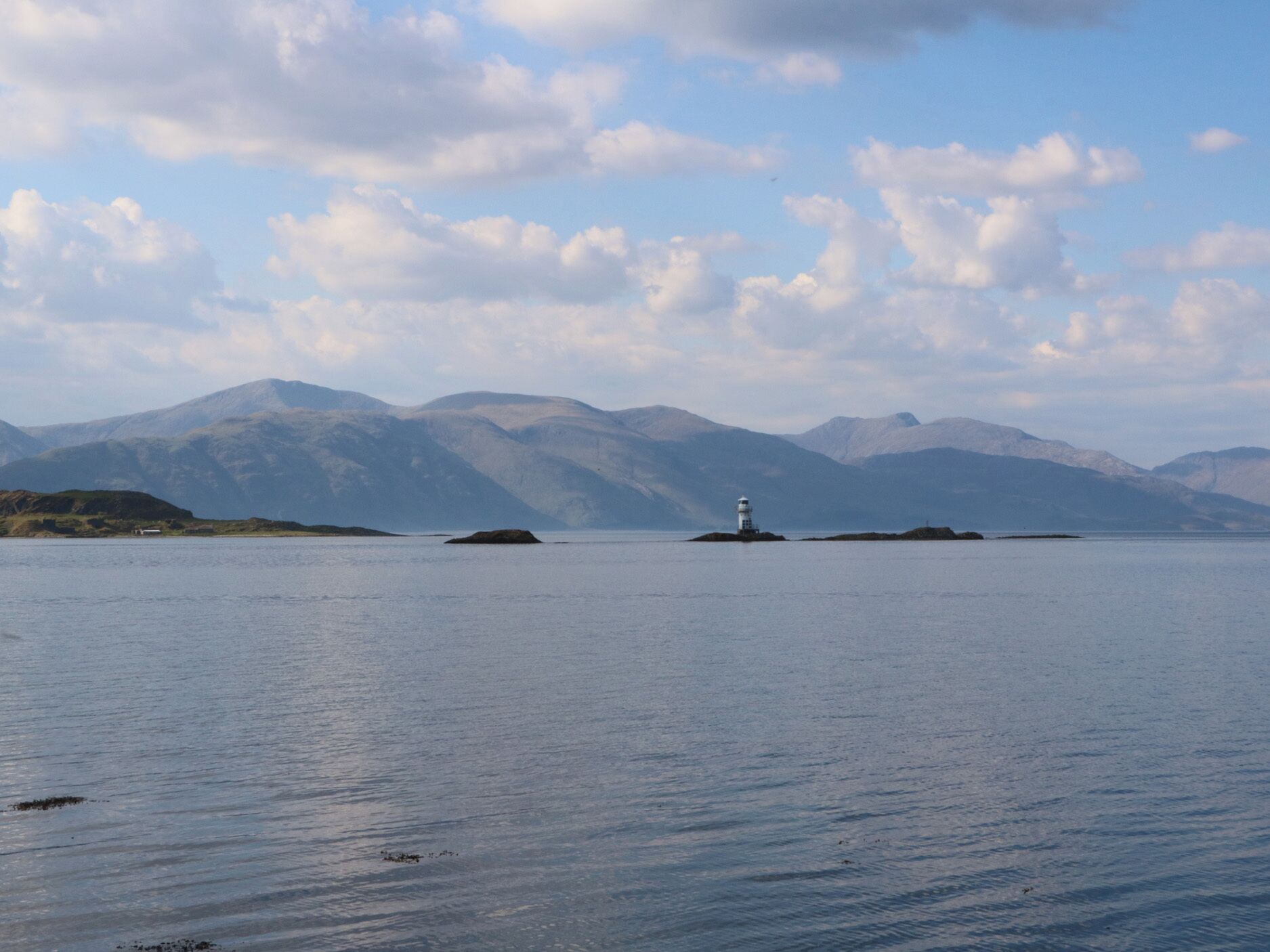 A calm lake with a lighthouse on an island, surrounded by mountains.
