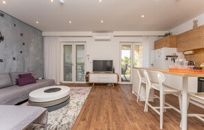 Ein modernes Wohnzimmer mit einer Couch, einem Fernseher, einem Essbereich mit Stühlen und einer Küche mit Schränken.
