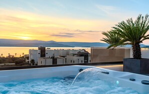 Ein Whirlpool mit Blick auf ein Gewässer und Berge bei Sonnenuntergang.