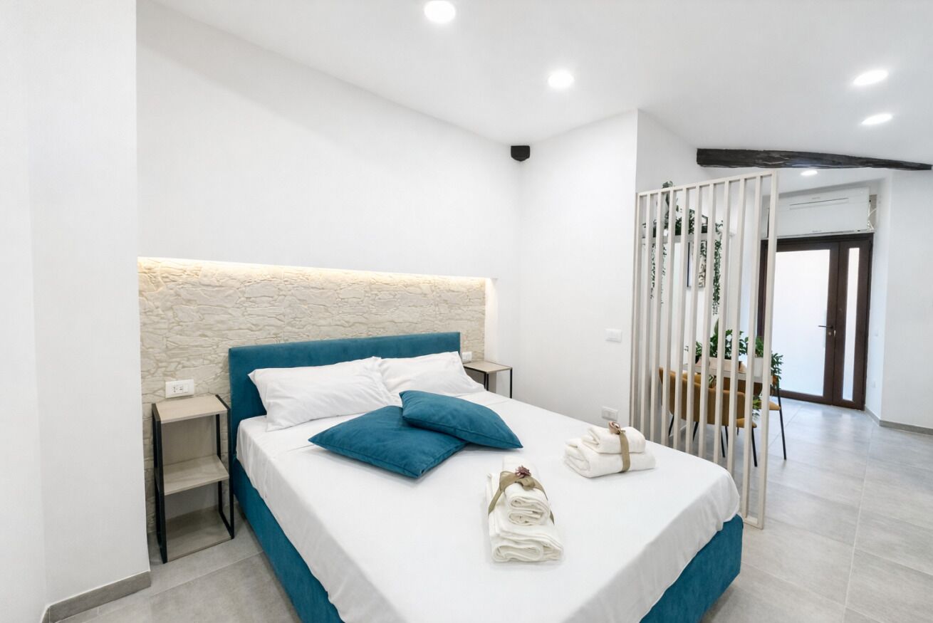 A modern bedroom with a stone-textured headboard, a neatly made bed with blue and white bedding, and a set of towels on the bed.