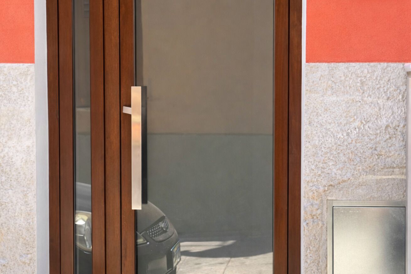 Una puerta con manija metálica y un panel de vidrio, que da a un estacionamiento donde se ve un coche a través del vidrio.