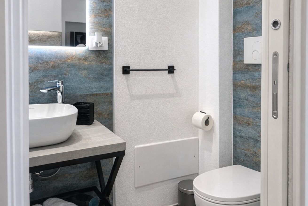 A bathroom with a white sink, a black towel rack, a toilet, and a mirror.