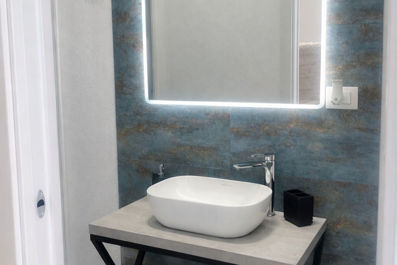A bathroom with a white sink, a rectangular mirror, and a wall-mounted light fixture.