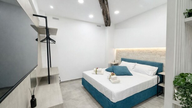 A modern bedroom with a bed, bedside tables, a hanging light fixture, and a plant. - Lulu Suite in the center (Cagliari)