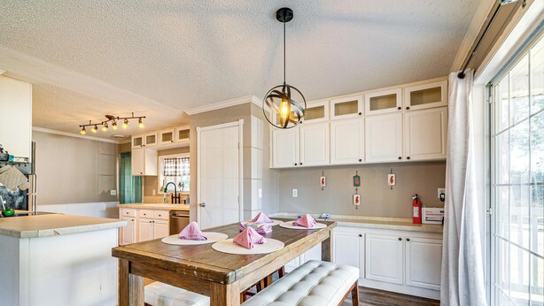 Una cucina moderna con mobili bianchi, un tavolo da pranzo in legno con tovaglioli rosa e una lampada a sospensione.