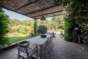 An outdoor patio with a table and chairs, surrounded by lush greenery and a view of a pool. - Villa-Superior-Ensuite-Park view- 3 chambres (La Garde-Freinet)