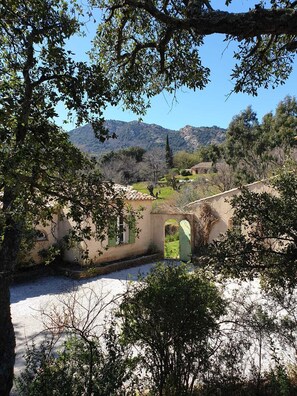 Un bâtiment rustique avec un pont de pierre, entouré d’arbres et adossé à un paysage montagneux.