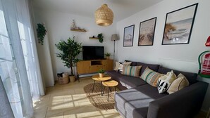 Ein modernes Wohnzimmer mit grauem Sofa, einem Holzbodenfernsehschrank, einer großen Pflanze und Kunstwerken an den Wänden.
