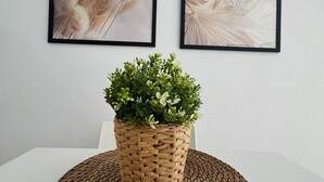 Ein Esstisch mit einer gewebten Tischmatte, einem Topfpflanzen und zwei gerahmten Kunstwerken an der Wand.
