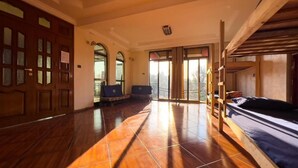 Une pièce spacieuse avec un plancher en bois, un lit superposé, un bureau avec une chaise et une grande fenêtre donnant sur l’extérieur.