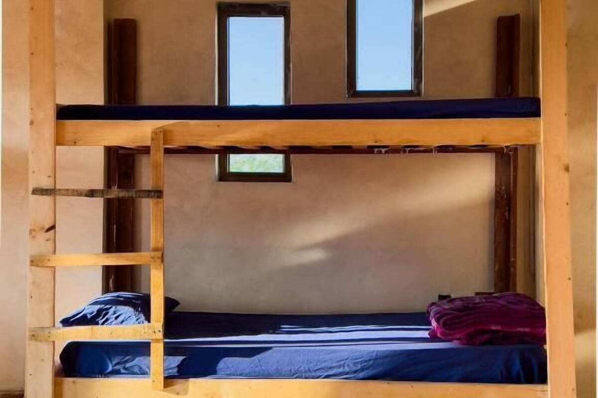 A bunk bed room with a wooden ladder, two small windows, and a tiled floor.