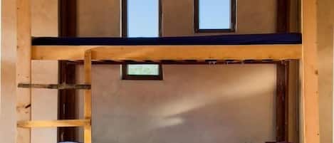 A bunk bed room with a wooden ladder, two small windows, and a tiled floor.