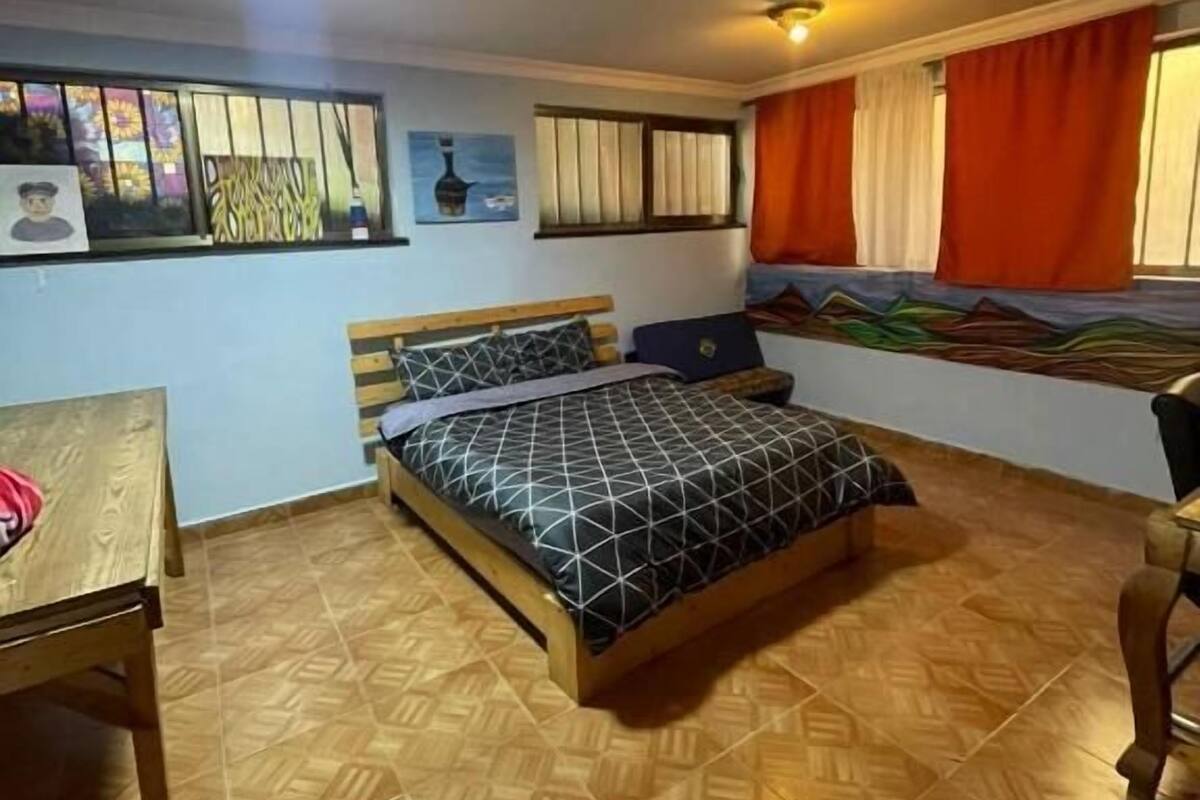 A bedroom with a bed, a wooden desk, and a window with curtains.
