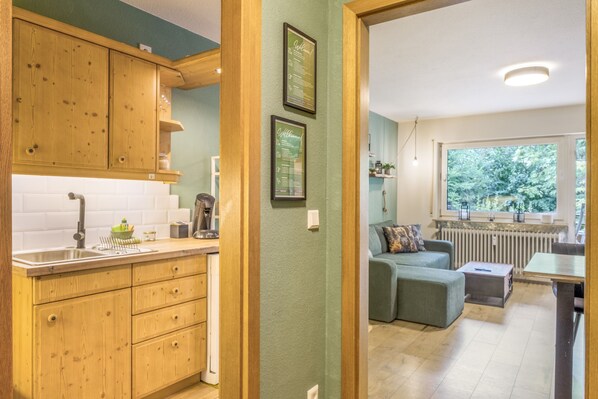 A kitchen with wooden cabinets, a sink, and a countertop. There is a framed welcome sign on the wall.