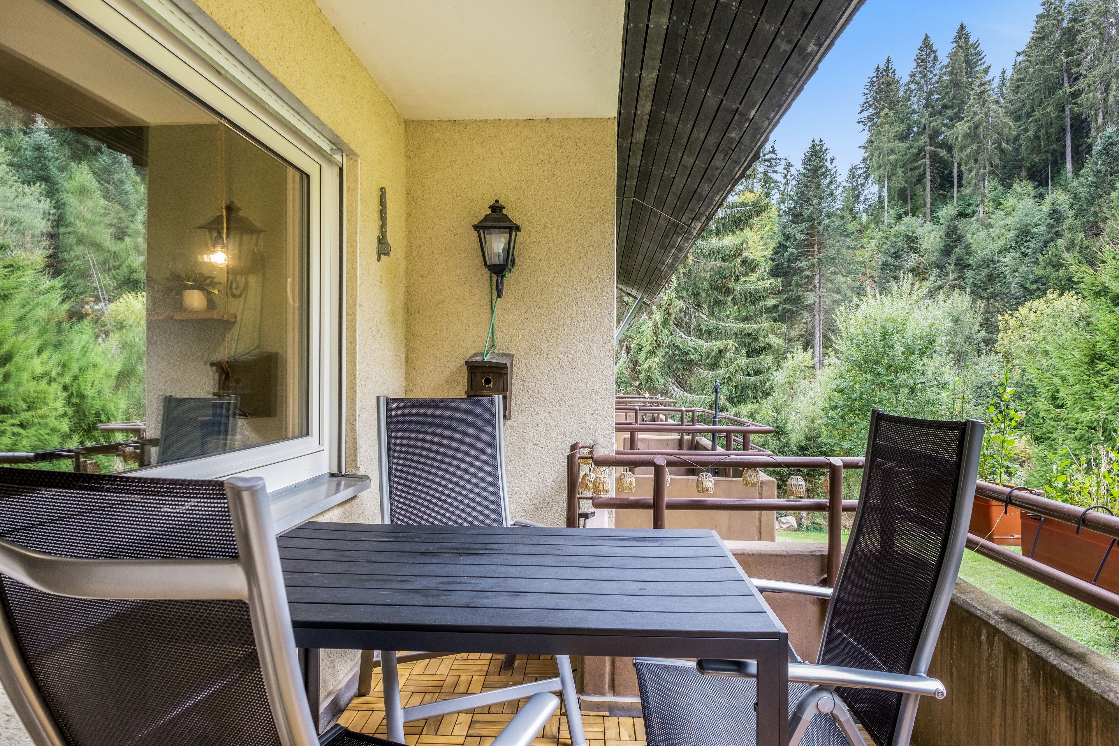 Ein Balkon mit Tisch und Stühlen, mit Blick auf ein bewaldetes Gebiet.