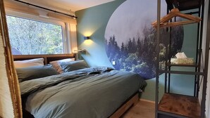 Quarto com cama, janela, luminária na parede e prateleira com caixa de lenços.